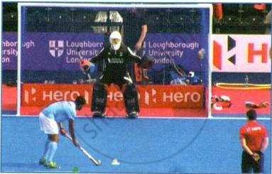 The image displays an educational photograph titled showing a field hockey penalty stroke situation with a player preparing to take the shot against a goalkeeper, overseen by an umpire.