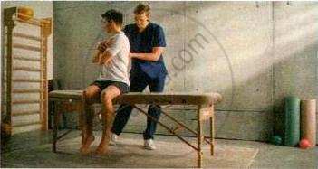 The image displays an educational photograph of a physical therapist assisting a seated athlete with a spinal or upper body stretch and adjustment exercise on a treatment table.